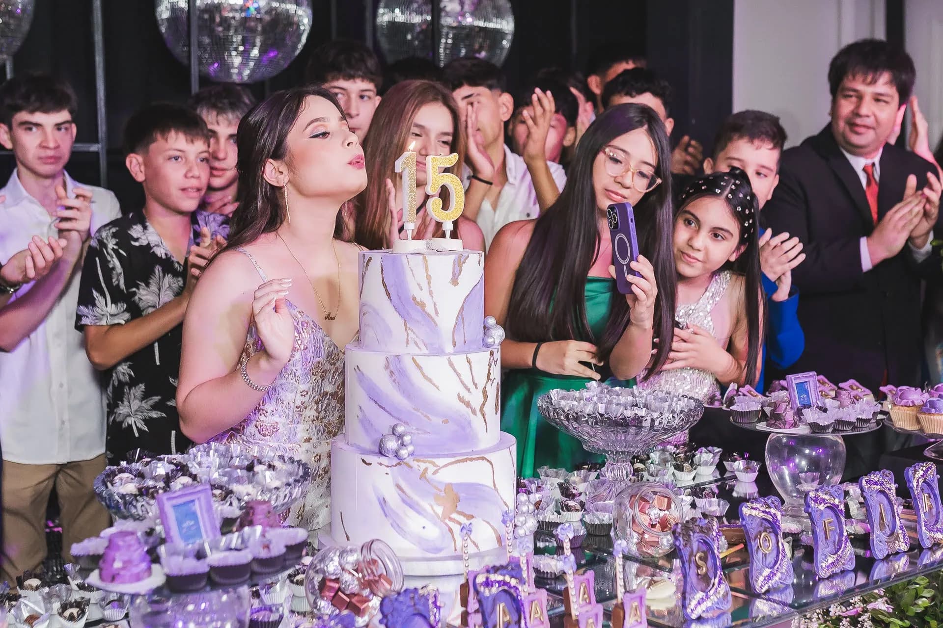 Quinceañera soplando la torta rodeada de amigos